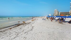 A beach with clear skies, a sandy shore, and a few people. There are umbrellas and lounge chairs, and a building is visible in the background. - Summit 0908A Romantic Gulf-View Studio at TOPS'L Resort (Miramar Beach)