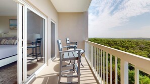 A balcony with a view of a forested landscape, a bed with a view, and two chairs. - Summit 0908A Romantic Gulf-View Studio at TOPS'L Resort (Miramar Beach)