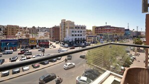 Una calle urbana concurrida con múltiples carriles de tráfico, varios edificios y cielo despejado.