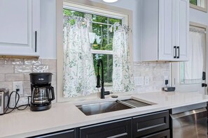 A modern kitchen with a coffee maker, a sink, and a window with curtains. - Tiny Home, HUGE Views, Massive Deck + Fire pit (Blairsville)