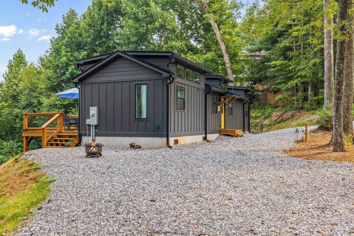 A cabin with a gravel driveway, a fire pit, and a wooden deck.