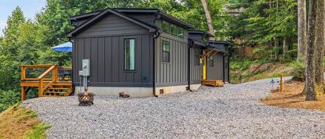A cabin with a gravel driveway, a fire pit, and a wooden deck.
