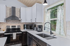 A modern kitchen with white cabinetry, a stainless steel range, a microwave, and a coffee maker. - Tiny Home, HUGE Views, Massive Deck + Fire pit (Blairsville)