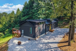 A cabin with a gravel driveway, wooden deck, and a small outdoor seating area. - Tiny Home, HUGE Views, Massive Deck + Fire pit (Blairsville)