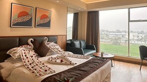 A modern hotel room with a large bed, a seating area, and a city view.