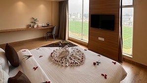 A hotel room with a large bed, a desk, a chair, a TV, and a view of the city.