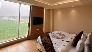 A bedroom with a large window, a bed with a decorative swan pillow, and a flat-screen TV mounted on the wall.