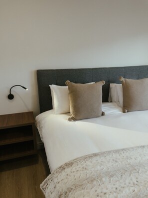 A neatly made bed with white linens and two textured pillows, a bedside table with a lamp, and a wooden nightstand. - One Bed Apt Modern Cozy Secure Sea Point (Cape Town)
