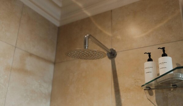 Un pommeau de douche avec un flexible, une étagère en verre pour les articles de toilette et un mur carrelé.