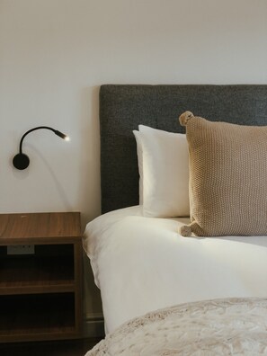 Un letto con un cuscino lavorato a maglia, una lampada da comodino e un comodino in legno.