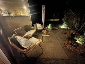 Et udendørs opholdsområde med fletmøbler og et bord, omgivet af planter og en sti.