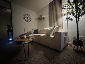 A living room with a sofa, a clock, a plant, and a table with a candle and a pumpkin. - Ferienwohnung in Kempten – Terrasse & Allgäu (Kempten (Allgäu))