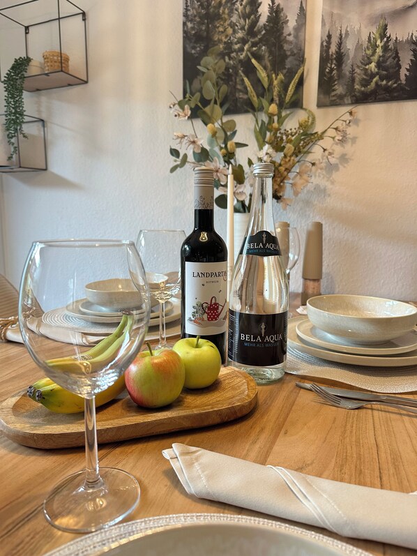 Et spisebord med vin, et glas, æbler og en skål med frugt.
