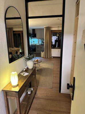 En gang der fører til et spiseområde med et bord dækket til to personer, et spejl, en lampe og en potteplante.