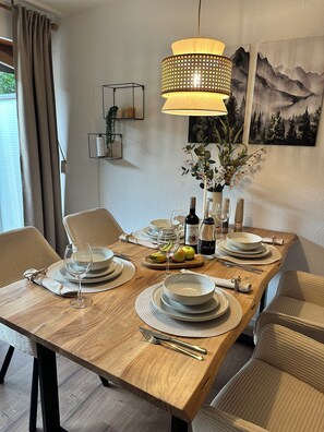 A dining table set with plates, glasses, cutlery, and a bottle of wine, with a hanging lamp above and a painting on the wall. - Ferienwohnung in Kempten – Terrasse & Allgäu (Kempten (Allgäu))