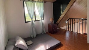 Une pièce avec un plafond en pente, un lit avec des oreillers, une table de chevet avec une lampe et une fenêtre avec des rideaux.