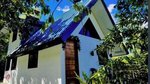 Un bâtiment blanc surmonté d’un toit bleu, entouré de verdure.