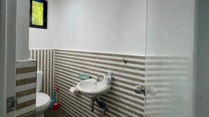 Une salle de bain avec un plafond en bois, un lavabo blanc, des toilettes et des carreaux muraux à rayures.