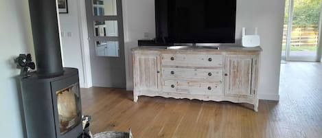 A living room with a wood-burning stove, a television on a cabinet, and a basket on the floor.