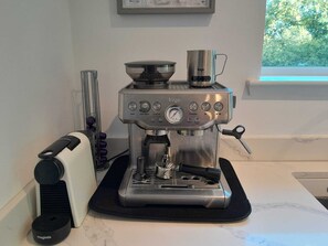En kaffemaskine i rustfrit stål på en køkkenbordplade med en sort måtte, en hvid brødrister og en kaffekværn.