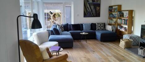 A living room with a sectional sofa, a small round table, a bookshelf, and a lamp.