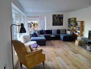 Ein Wohnzimmer mit Ecksofa, einem kleinen runden Tisch, einem Bücherregal und einer Lampe.