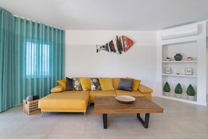 A modern living room with a yellow sofa, a wooden coffee table, and a decorative wall piece.