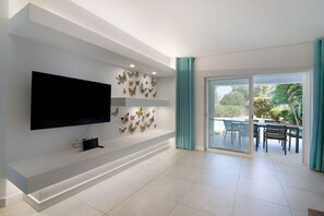 A modern living room with a flat-screen TV, decorative butterfly wall art, and a sliding glass door leading to an outdoor dining area.