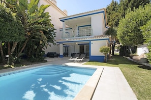 A two-story building with a swimming pool, outdoor seating, and lush greenery.