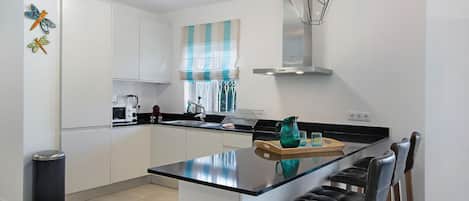 Una cocina moderna con una isla central, taburetes de bar y una lámpara colgante.