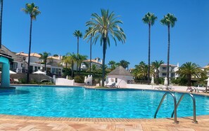 A swimming pool with clear blue water, surrounded by palm trees and lounge chairs. - Beautiful 2-Bedroom Apartment with Private Pool and Garden in Quinta do Lago (Faro)
