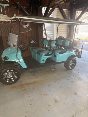 Ein türkisfarbenes Golfmobil steht in einer Garage mit Metall- und Holzwänden.