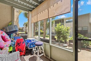 En balkon med udsigt over et boligområde, en fletstol og en blå køleboks.