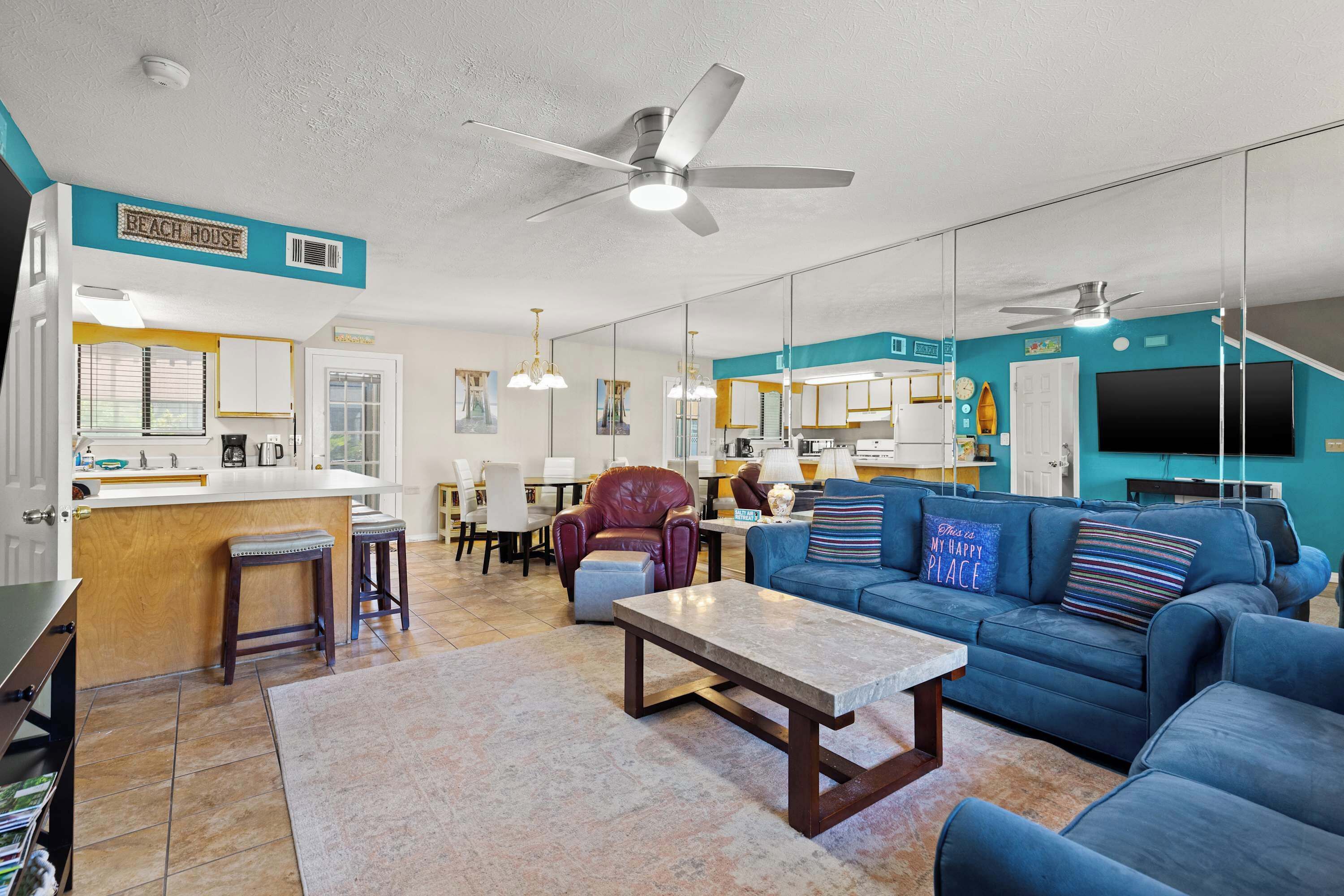 A modern living room with a blue sofa, a coffee table, and a dining area with a kitchen in the background.