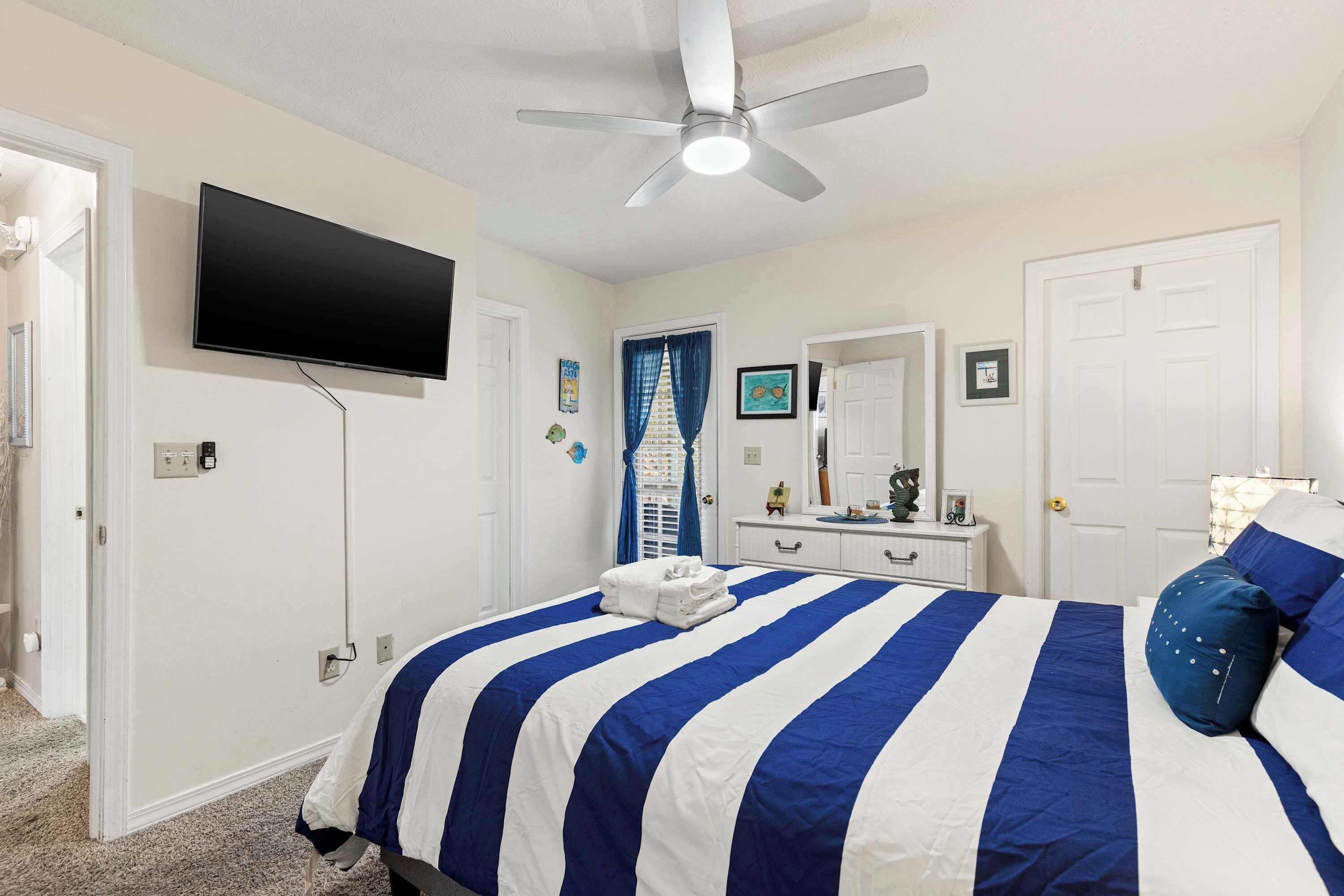 A bedroom with a bed, a ceiling fan, a TV mounted on the wall, and a door.