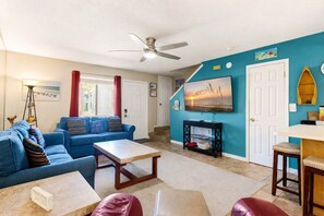Un salon avec un canapé bleu, une table basse, un téléviseur et un ventilateur de plafond.