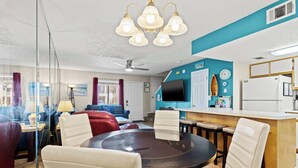 A modern living room with a dining area, a ceiling fan, and a TV mounted on the wall. - Resort Townhome with Private Patio near Beach (Panama City Beach)