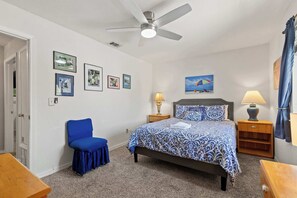 Ein Schlafzimmer mit einem Bett, einem Sessel, einem Deckenventilator und einem Bild an der Wand.
