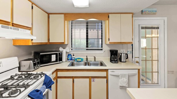 A compact kitchen with a gas stove, microwave, toaster, sink, and a window with blinds. - Resort Townhome with Private Patio near Beach (Panama City Beach)