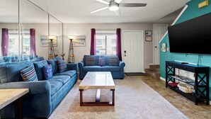 A living room with a ceiling fan, two sofas, a coffee table, and a television on a stand. - Resort Townhome with Private Patio near Beach (Panama City Beach)