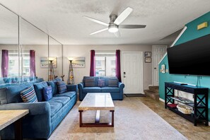 Ein Wohnzimmer mit Deckenventilator, zwei Sofas, einem Couchtisch und einem Fernseher auf einem Schrank.