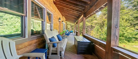 A covered porch with wooden flooring, a bench, and a table with chairs.