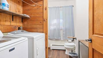 A compact bathroom with wooden walls, a washing machine, a toilet, and a shower curtain.