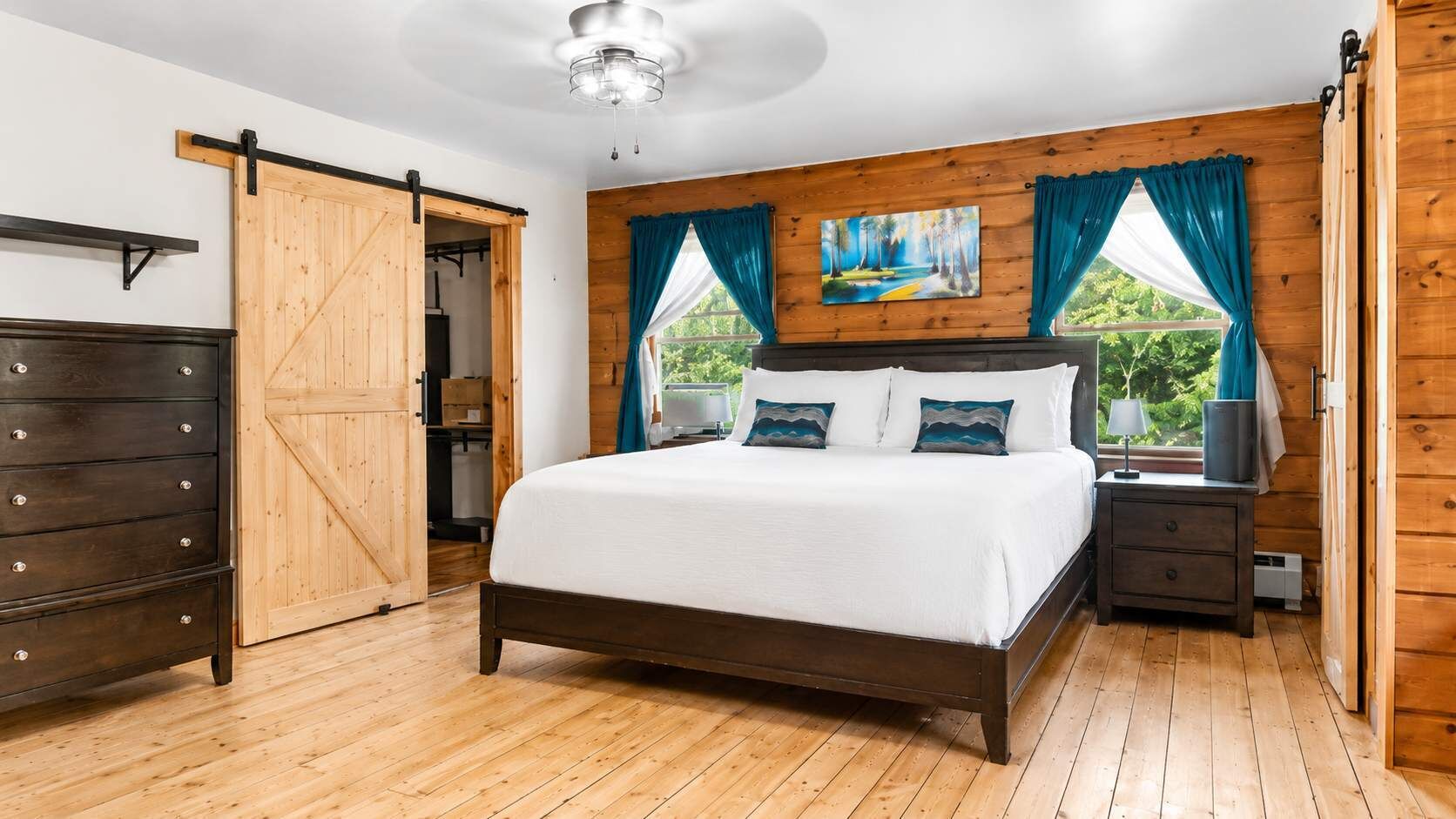Une chambre avec un plancher en bois, un lit avec une literie blanche, une table de chevet, une lampe, un tableau au mur et une porte coulissante.