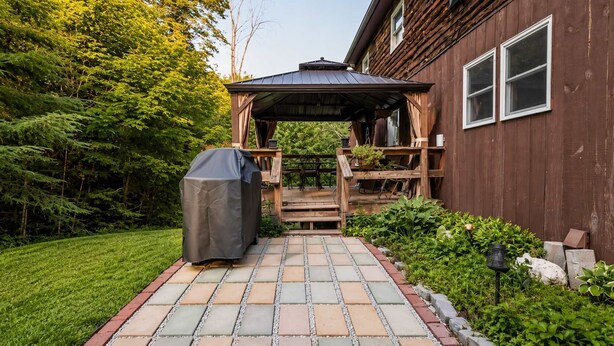 En træterrasse med en overdækket siddekrog, grill og en sti til et hus med træfacade.