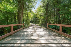 A wooden bridge with railings, surrounded by dense green foliage. - Riverfront Log Home - 28 Acres - Fire Pit (Warner)