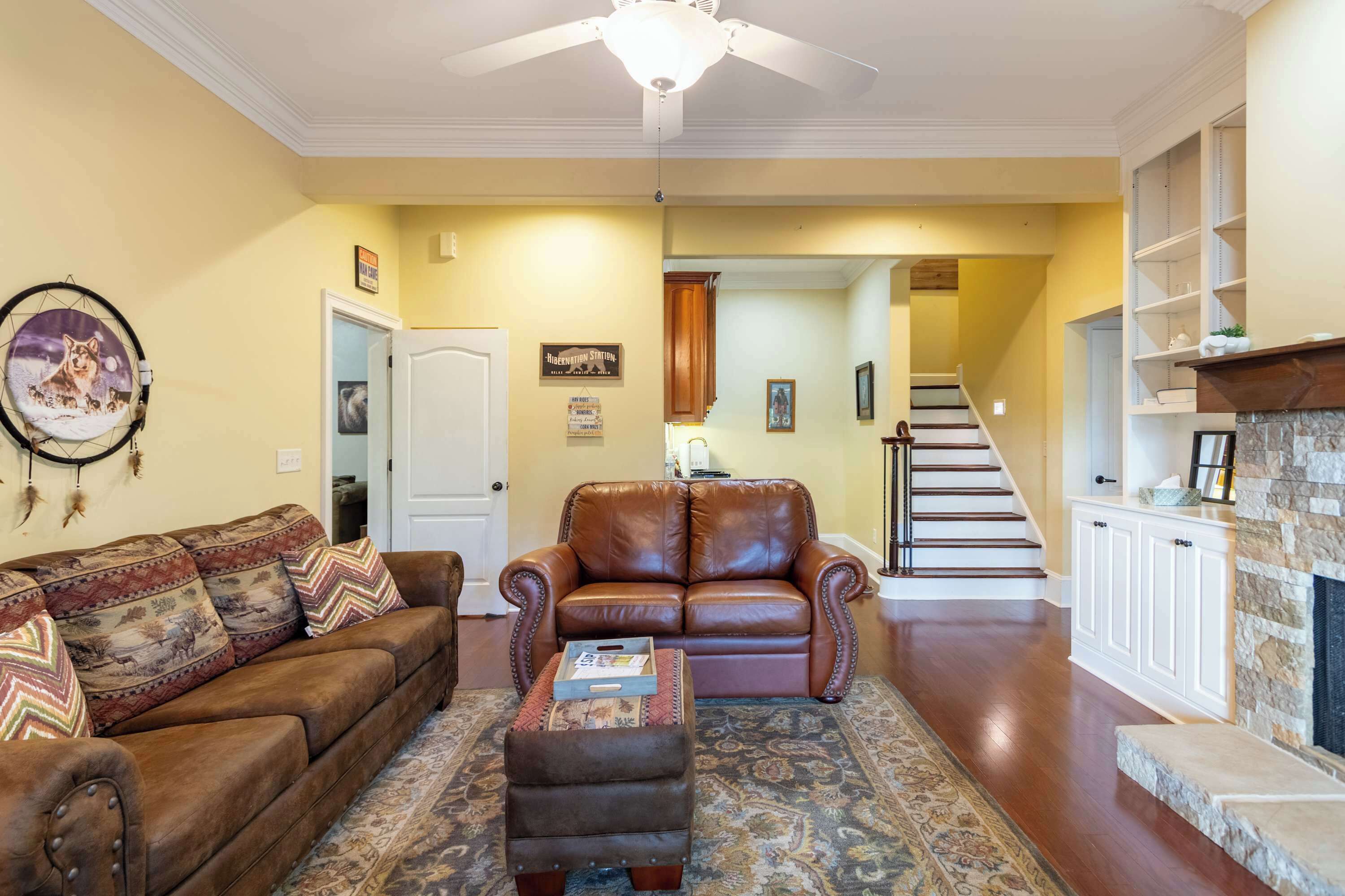 A living room with a brown leather sofa, a patterned ottoman, and a ceiling fan.