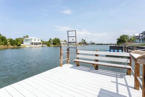 A wooden dock with a bench, a basketball hoop, and a view of a calm lake with houses in the background. - Hernando Beach 3BR - Water Views, Fireplace (Hernando Beach)