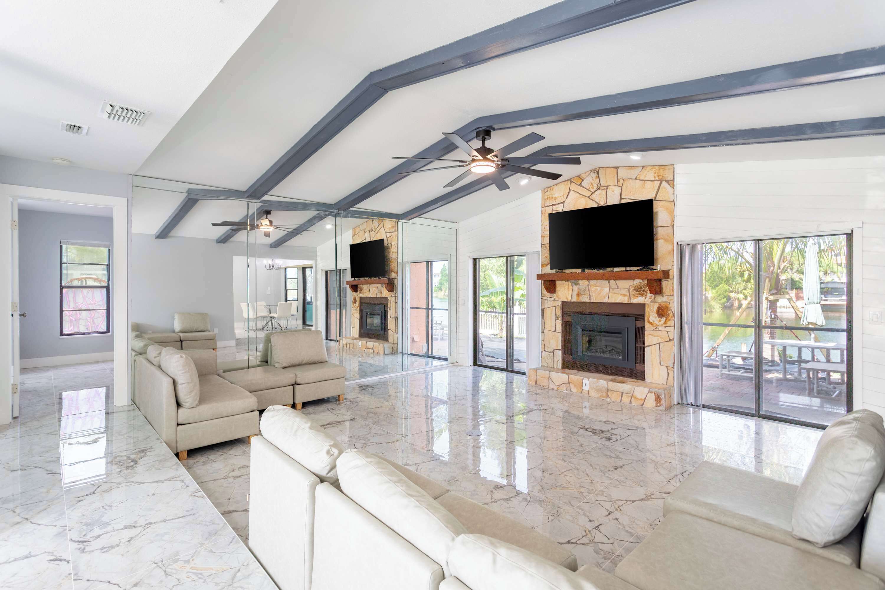 A spacious living room with a stone fireplace, ceiling fans, and large windows.