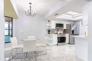 A modern kitchen with white cabinetry, a stainless steel refrigerator, a built-in oven, and a glass dining table with white chairs. - Hernando Beach 3BR - Water Views, Fireplace (Hernando Beach)